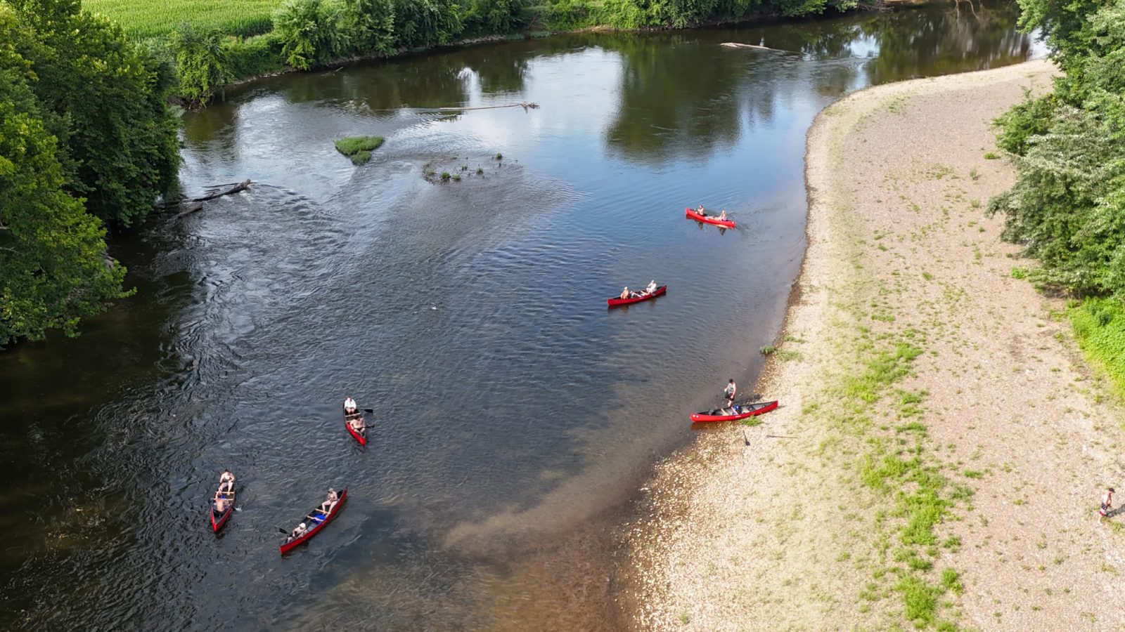 A group of red canoes paddling the Tuscarawas River past a gravel bar in Coshocton, Ohio
